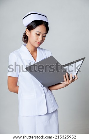 Young Asian nurse read data in a ring binder on gray background