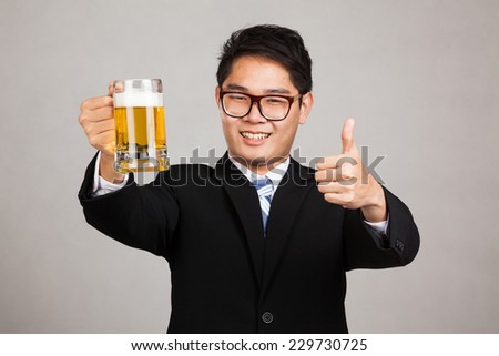 Asian businessman thumbs up with mug of beer on gray background