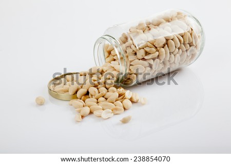 Peeled peanuts in jar on white  table with lid off