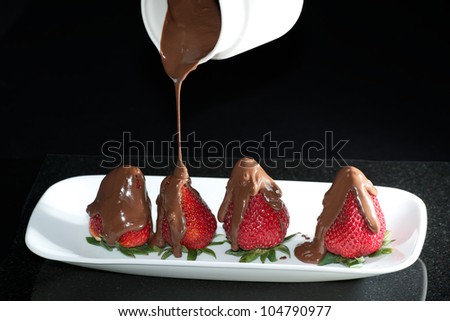 Pouring melted chocolate over fresh strawberries on white plate.