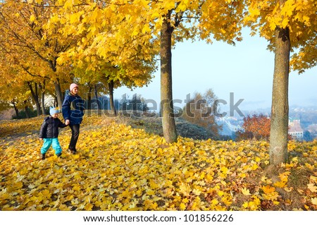 Happy family (mother with small son) walking in golden maple autumn park