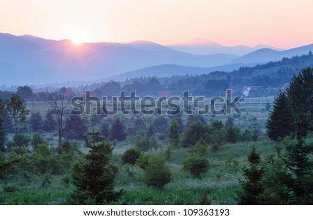 Beautiful summer country landscape with setting sun over mountains