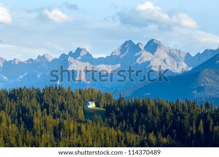 Summer evening mountain view with fir forest and house on hill and Tatra range behind (Poland)