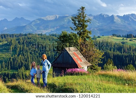 Summer evening mountain village outskirts with wooden shed and family to walk and Tatra range behind (Gliczarow Gorny, Poland)