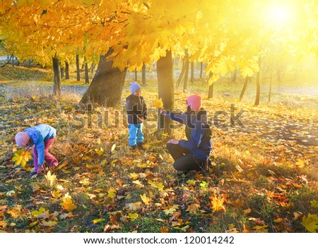Happy family (mother with small children) walking in golden maple autumn park and sunshine behind the tree foliage