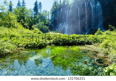 Summer view of large waterfall and clear lake with green plants at the bottom (Plitvice Lakes National Park, Croatia)