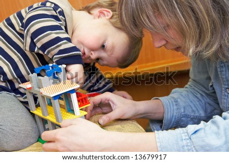 Mother with small son play with building set for children (built a house)