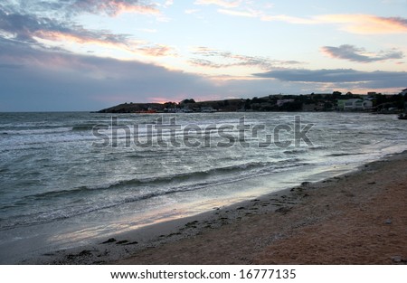 Evening sandy sea coast and small port far away