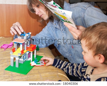 Mother with small son play with building set for children (built a house)