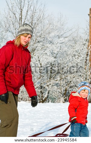 Happy family (mother with small boy) on winter snow covered courtyard near house