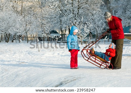 Happy family (mother with small boy and girl) on winter snow covered courtyard near house