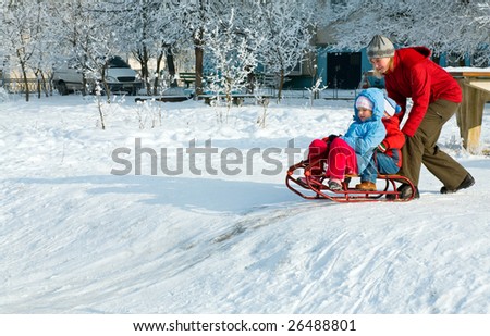 Happy family (mother with small boy and girl) on winter snow covered courtyard near house