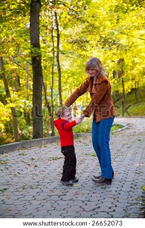 Happy family (mother with small boy) funny dance in golden autumn city park