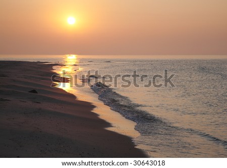 misty daybreak sea sandy shore with sunlight path and fishing boat distant silhouette