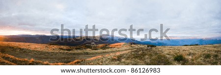 Autumn evening plateau landscape with lust golden-pink sunlight on mountains and evening glow in sky.