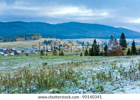 First winter snow on October Carpathian mountain plateau with mountain village and highway far away