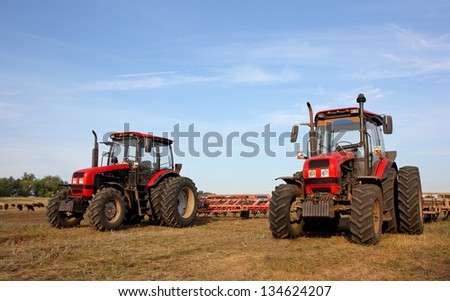 Color photo of two red tractors with a harrow