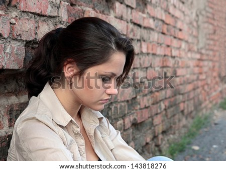 Young woman in despair sitting against a brick wall