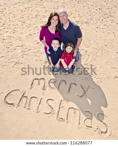 Family write Merry Christmas greeting in beach sand