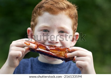 Boy eating a BBQ rib outside getting messy