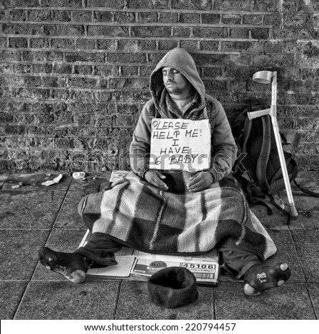 LONDON, UK - AUG 22, 2014: Homeless man with an asking for help sign sleeping in tunnel outside Waterloo train station in London in black and white.