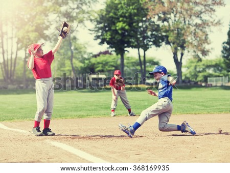 Boy sliding into base during a baseball game with Instagram style filter, focus is on catcher.