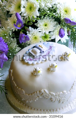 A christening cake in front of a flower arrangement