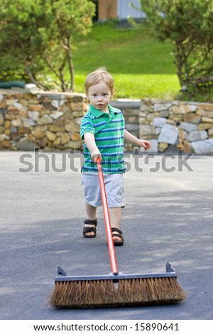 Boy with yard brush cleaning driveway outside