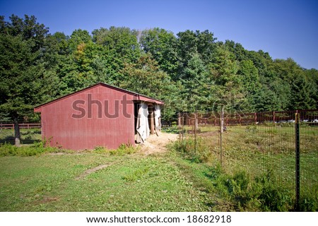 Old run down wooden barn in front of trees and fence