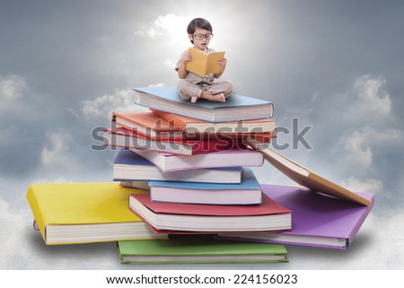 Little boy reading a book on pile of books