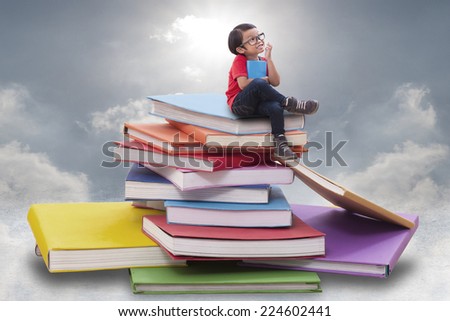 Little boy holding a book and sitting on pile of books