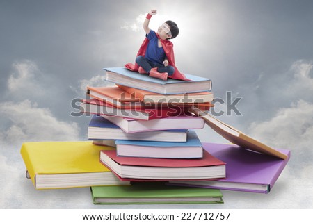 Superhero boy child sitting on pile of books