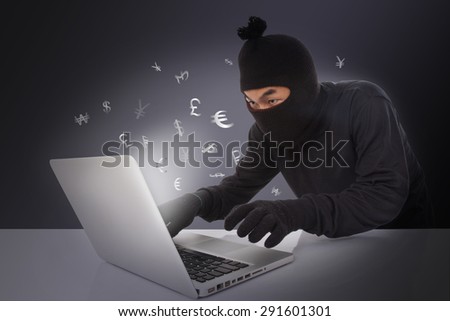 Computer hacker wearing mask stealing data on laptop computer
