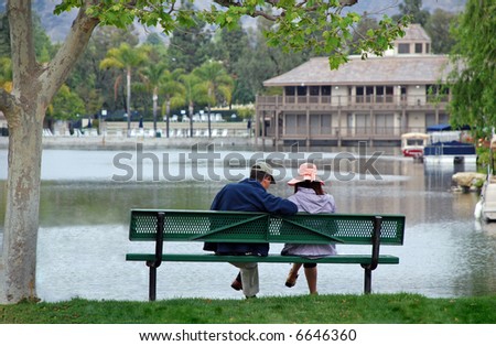 A couple sit on a bench by a lake, contemplating future plans.