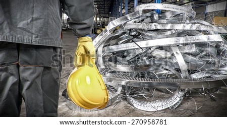 worker with helmet in production hall in front of steel sheet metal scrap
