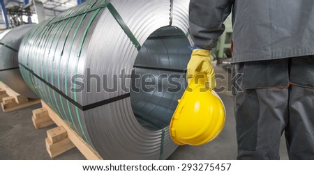 worker with protective helmet and protective gloves in front of tin metal rolls
