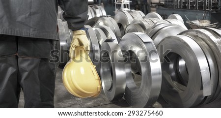 worker with protective helmet and protective gloves in front of tin metal rolls
