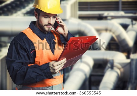 worker in protective uniform with smart phone and clipboard in front of industrial pipes - toned image, retro film filtered in instagram style