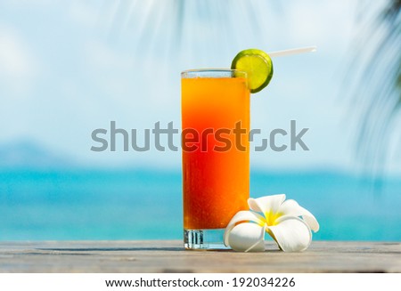Tropical orange cocktail with Plumeria or Frangipani flower on the sea background