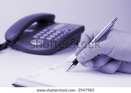Man holding pen and writing in weekly planner, phone on the background