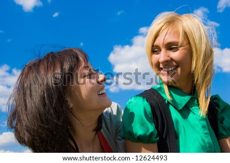 Two laughing girls look face to face on the sky background
