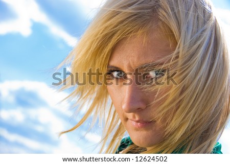 Stylish cute blonde with fly-away hair. Portrait on sky background.