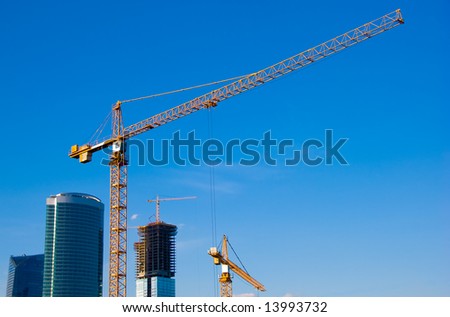 Sky-scrapers construction. Cranes and buildings over blue sky.