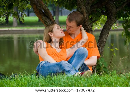Loving couple kisses under a tree on a river bank