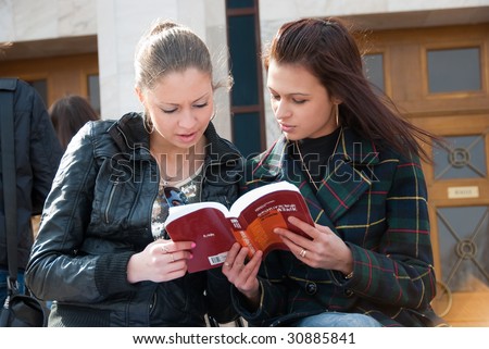 Two cute students read textbook outdoors