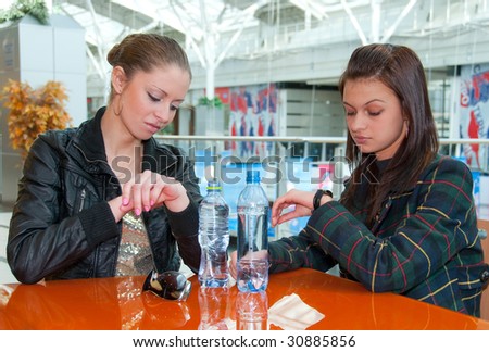 Two girls looking to watches sitting in a food court in a mall