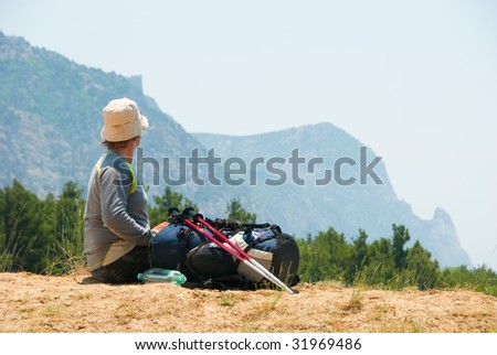 Tired hiker relaxes on a hill and enjoys landscape