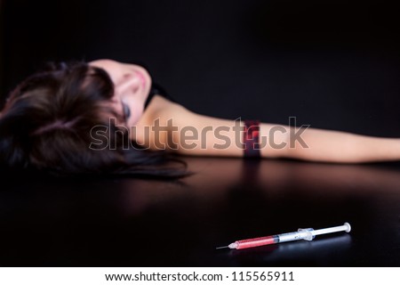 Drug addict woman with syringe is sleeping on table. Simulated, studio shot. Focus is on the syringe