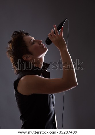 Young woman with microphone on gray background