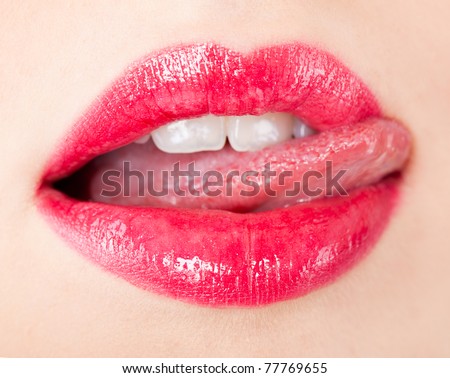 Close-up of a female mouth with big red lips and white teeth which she touches with her tongue